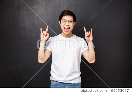 Carefree outgoing young male student having fun at awesome party at dorm, listening cool music at festival, make rock-n-roll gesture smiling and dancing, standing black background 63353667