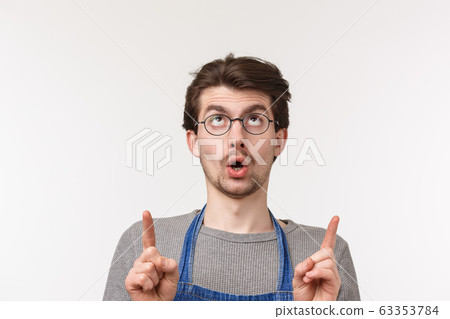 Advertisement, small business and career concept. Close-up portrait of curious and intrigued caucasian man in apron and glasses spot something interesting upwards, pointing fingers up Advertisement, small business and career concept. Close-up portrait of curious and intrigued caucasian man in apron and glasses spot something interesting upwards, pointing fingers up 63353784