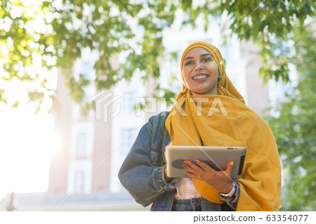 Arab woman student. Beautiful muslim female student wearing bright yellow hijab holding tablet. 63354077