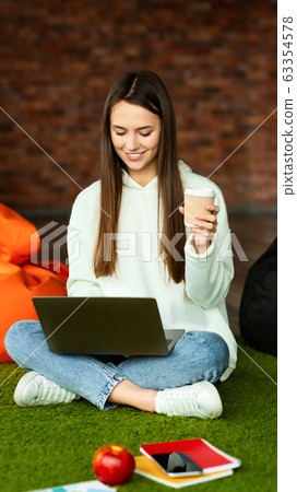 Girl in workspace working on laptop and drinking coffee 63354578
