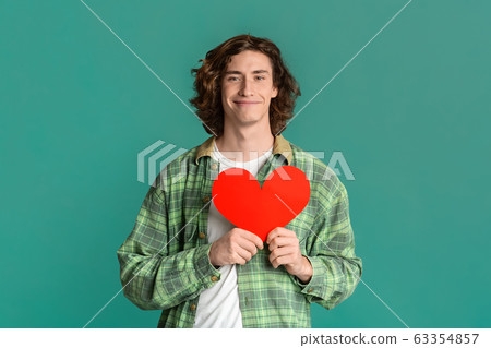 Expressing love. Romantic young guy with red paper heart on color background Expressing love. Romantic young guy with red paper heart on color background 63354857