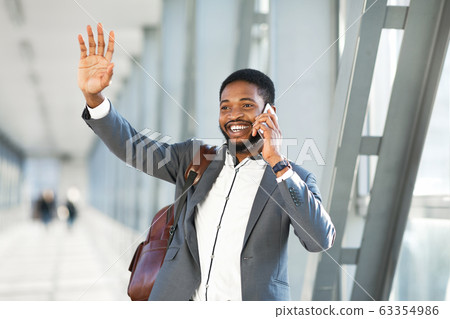 Happy Businessman Waving Hand Talking On Cellphone Walking In Airport Happy Businessman Waving Hand Talking On Cellphone Walking In Airport 63354986