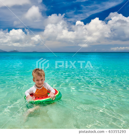 Toddler boy on beach swimming with inflatable ring 63355293