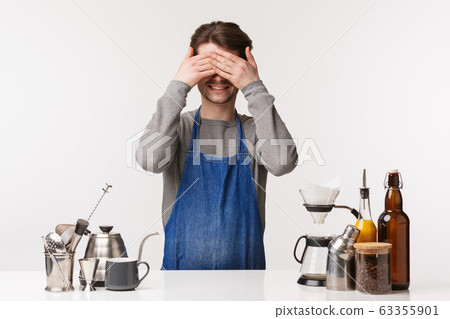 Barista, cafe worker and bartender concept. Funny and cute young male employee having fun during break, standing apron near bar counter with teapots, making coffee, close eyes and smiling 63355901