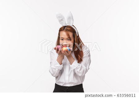 Easter holiday, celebration concept. Portrait of funny asian woman in rabbit ears, holding greedy and amazed at painted eggs as if telling my precious, standing entertained white background 63356011