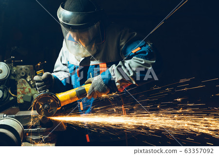 Locksmith in special clothes and goggles works in production. Metal processing with angle grinder. Sparks in metalworking 63357092