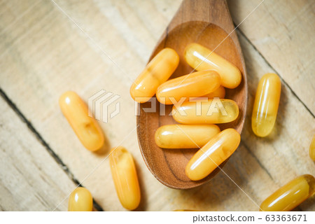 Royal jelly capsules in wooden spoon and wood 63363671