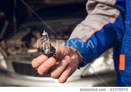 Car service men. Replacing a burnt out lamp in the car headlight Car service men. Replacing a burnt out lamp in the car headlight 63370974