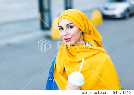 Young beautiful arab woman in hijab drinking cooling cocktail outdoor. 63373140