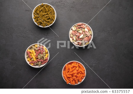 Various types of pasta on in multicolored bowls and scattered on classic dark rustic backgroun 63375557