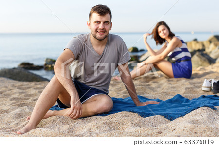 Man sitting on the beach. Girl on the background Man sitting on the beach. Girl on the background 63376019