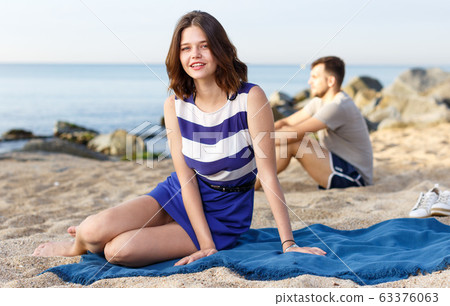 Girl sitting on the beach. Man on the background Girl sitting on the beach. Man on the background 63376063