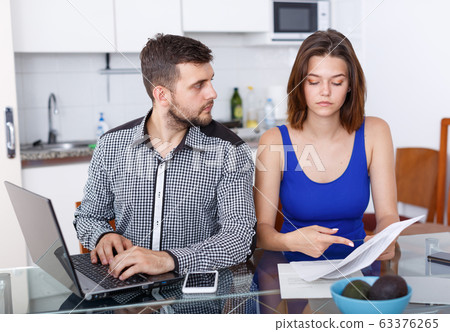 Serious young family couple with documents using laptop Serious young family couple with documents using laptop 63376265