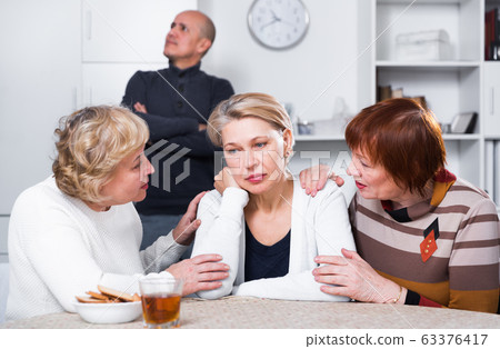 Mature woman is sitting upset and her girlfriends are expressioning understanding to she 63376417