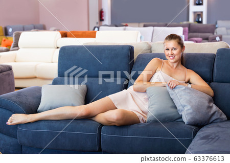 Woman buyer lying barefoot with pillow on the sofa in furniture shop 63376613
