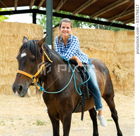 Young woman riding a horse on a farm 63376617