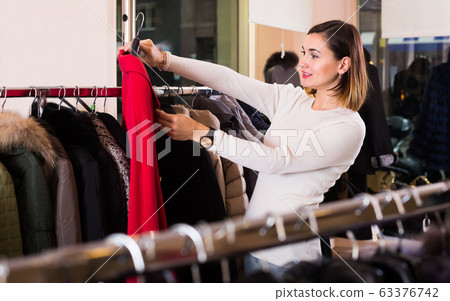 Charming female customer examining red woolen coat Charming female customer examining red woolen coat 63376742