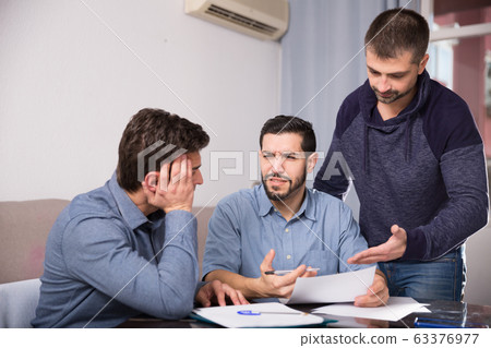 Three troubled men discussing documents at desk Three troubled men discussing documents at desk 63376977