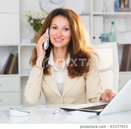 Businesswoman is working with laptop and talking by phone on her workplace Businesswoman is working with laptop and talking by phone on her workplace 63377053