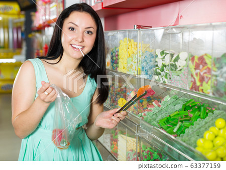 Pretty girl in sweets store picks up candies in bag Pretty girl in sweets store picks up candies in bag 63377159