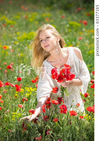 Young girl in white dress picking poppies plants outdoor in fields Young girl in white dress picking poppies plants outdoor in fields 63377165