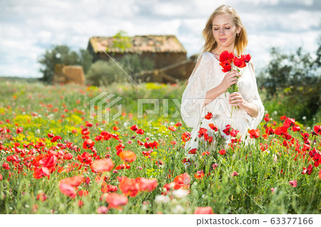 Woman wearing white dress holding bouquet of poppy flowers in fields Woman wearing white dress holding bouquet of poppy flowers in fields 63377166