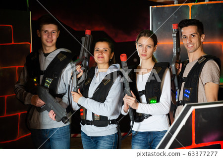 Four happy young men an women posing with laser pistols in their hands in dark laser tag room 63377277