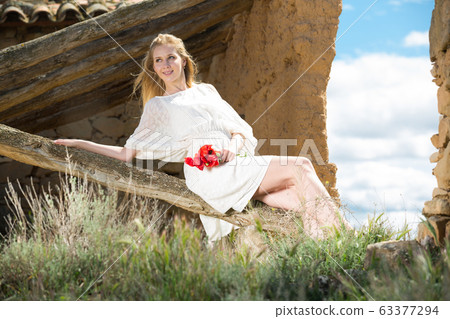 Beautiful woman wearing white dress sitting with poppies flowers Beautiful woman wearing white dress sitting with poppies flowers 63377294