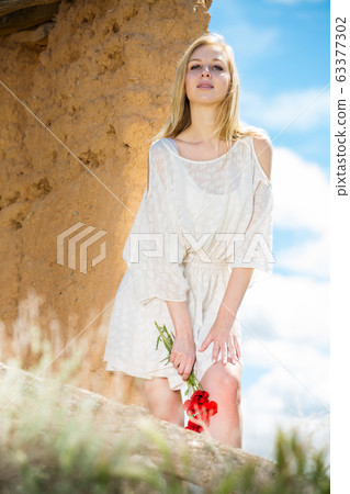 Woman wearing white dress posing near wall with poppies flowers Woman wearing white dress posing near wall with poppies flowers 63377302