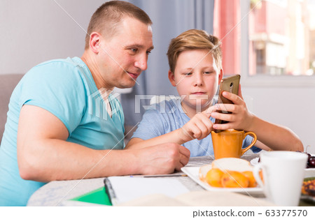 Man with his son are playing on phone together Man with his son are playing on phone together 63377570