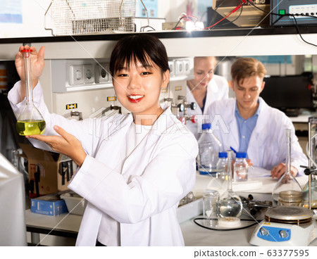 Young Asian female student viewing flask of liquor at chemical lab Young Asian female student viewing flask of liquor at chemical lab 63377595