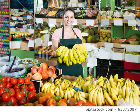 Portrait of smiling saleswoman with cluster of yellow bananas in store 63378097