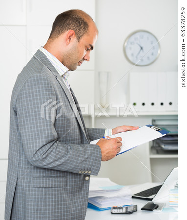 Man working in the office at the laptop with documents Man working in the office at the laptop with documents 63378259