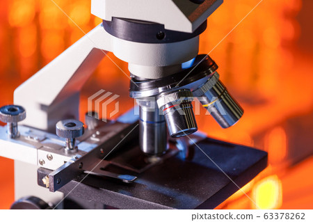 Close up of microscope lenses focused on a specimen in warm orange light light. Close up of microscope lenses focused on a specimen in warm orange light light. 63378262