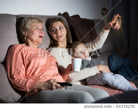 Woman with her mother and son are watching film in time evening rest Woman with her mother and son are watching film in time evening rest 63378270
