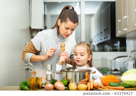 Daughter helping cooking soup and mother add pepper to pan Daughter helping cooking soup and mother add pepper to pan 63378427