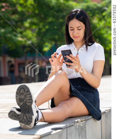 Young positive girl chatting on phone in the city center 63378582