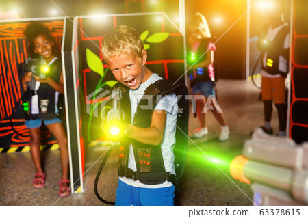 Excited little boy aiming laser gun at other players during lase Excited little boy aiming laser gun at other players during lase 63378615