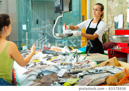 Glad female weighing raw prawns on scales 63378936