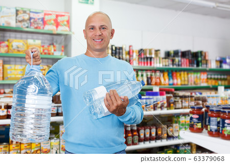 Positive man customer buying still water in bottles in grocery shop 63379068