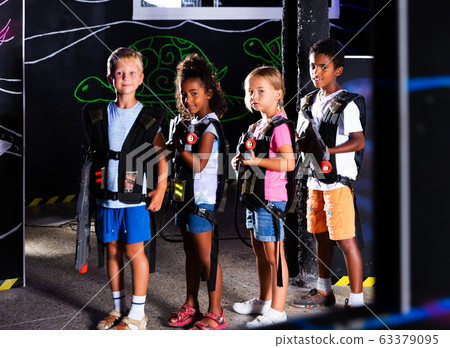 Group portrait of positive smiling teenagers with laser guns having fun on dark lasertag arena 63379095