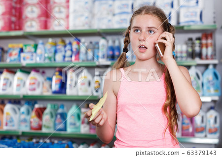 Girl choosing products with shopping list and talking by smartphone Girl choosing products with shopping list and talking by smartphone 63379143
