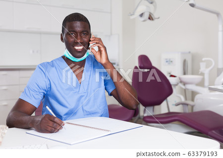 Dentist african american talking on mobile phone in office Dentist african american talking on mobile phone in office 63379193