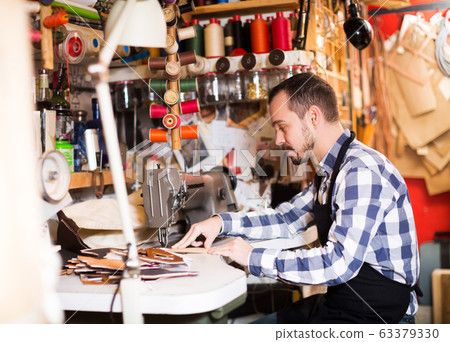 Male worker stitching new belt 63379330
