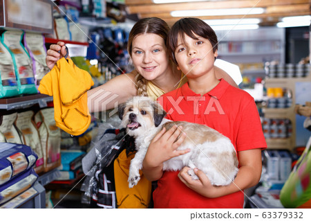 Teen boy with mother choosing dog clothes for their puppy in pet supplies store 63379332