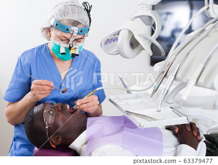 Dentist is treating male patient which is sitting in dental chair Dentist is treating male patient which is sitting in dental chair 63379477