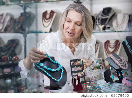 Woman jewelry store seller puts necklaces and earrings on the counter Woman jewelry store seller puts necklaces and earrings on the counter 63379490