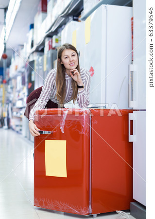 Positive woman seller suggesting refrigerator in store Positive woman seller suggesting refrigerator in store 63379546
