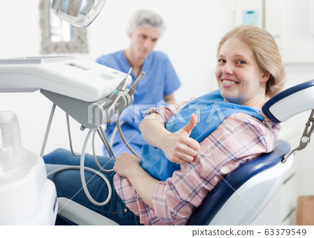 Client woman is sitting satisfied in chair after treatment in dental office Client woman is sitting satisfied in chair after treatment in dental office 63379549