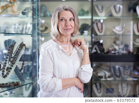 Adult woman trying on a rose quartz necklace and earrings at a jewelry store Adult woman trying on a rose quartz necklace and earrings at a jewelry store 63379572